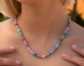 May include: A colorful beaded necklace with round, multi-colored beads. The necklace is made of agate and is worn by a person with short blonde hair.