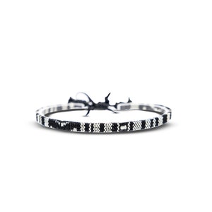 May include: A black and white woven bracelet with a black string tie closure.
