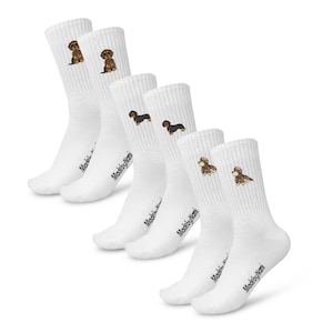 May include: Set of six white crew socks with embroidered dachshund designs. The socks feature the text "MadebyNomi" on the bottom of each sock.