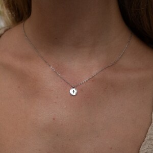 May include: A silver chain necklace with a small, round pendant featuring a cross cutout.