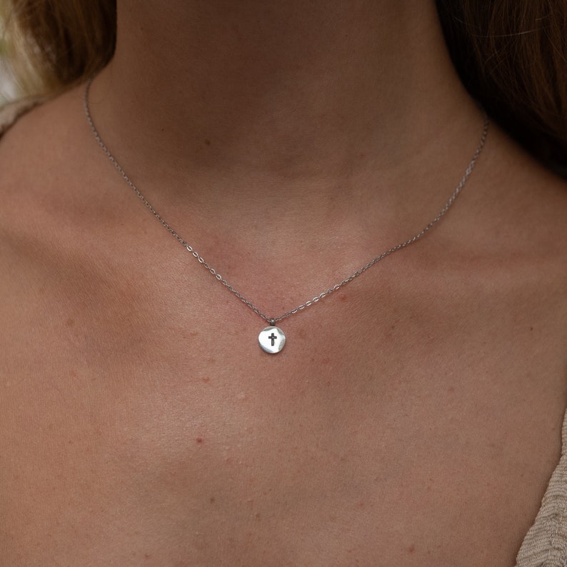 May include: A silver chain necklace with a small, round pendant featuring a cross cutout.