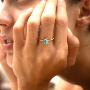 Pode incluir: Um anel de ouro com uma pedra oval turquesa engastada no centro. O anel tem uma banda torcida.