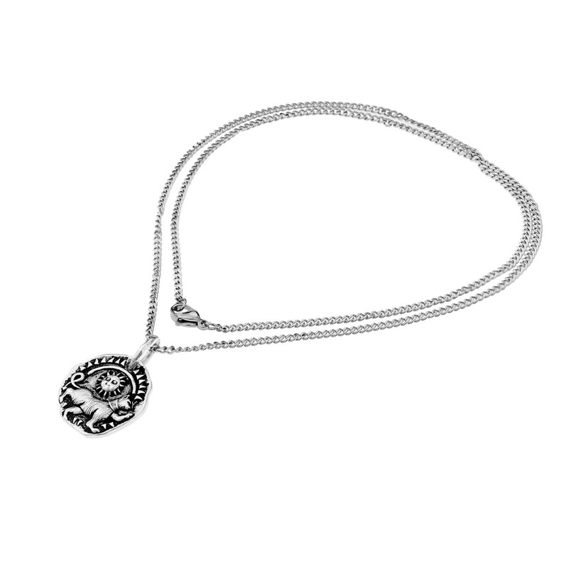 Pu&ograve; includere: Collana color argento con un ciondolo con un design dettagliato di un leone e un sole. Il ciondolo ovale &egrave; appeso a una delicata catena. La collana &egrave; esposta su uno sfondo bianco.