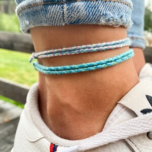Puede incluir: Dos tobilleras, una es azul claro con un toque de amarillo y la otra es rosa claro con un toque de azul.