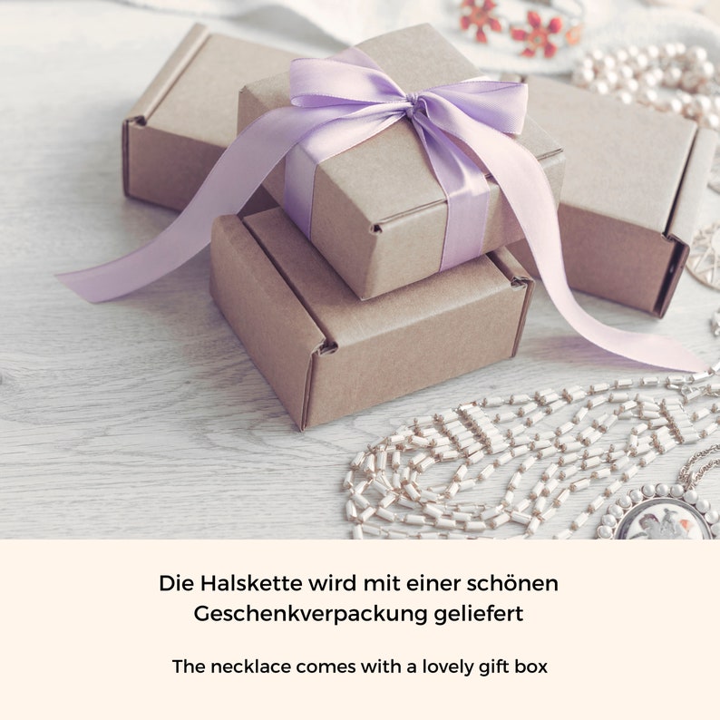 K&ouml;nnte beinhalten: Eine Geschenkbox mit einem lila Band und einer kleineren Geschenkbox im Inneren. Die Geschenkboxen stehen auf einer Holzoberfl&auml;che mit einer Perlenkette.