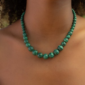 Könnte beinhalten: Eine grüne Malachit-Perlenkette mit runder Form. Die Perlen sind alle gleich groß und auf einer dünnen Schnur aufgefädelt.