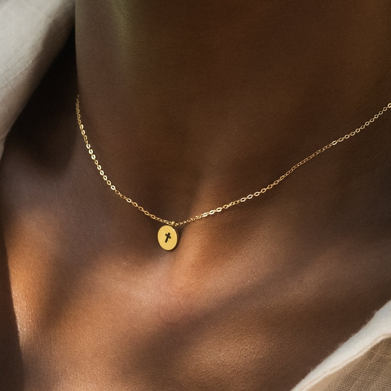 May include: A gold chain necklace with a small round pendant featuring a cross design.