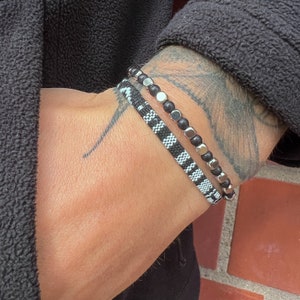 May include: Two bracelets on a wrist. One bracelet is black and white checkered, the other is silver with black beads.