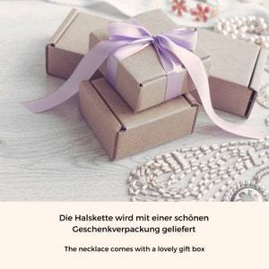 May include: A gift box with a purple ribbon and a smaller gift box inside. The gift boxes are sitting on a wooden surface with a pearl necklace.