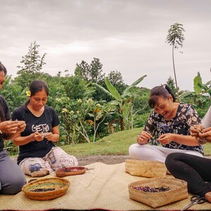 Puede incluir: Cuatro personas est&aacute;n sentadas en una estera tejida al aire libre, haciendo pulseras con cuentas de colores. Llevan ropa informal y est&aacute;n rodeadas de vegetaci&oacute;n.