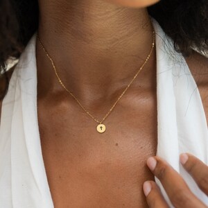 May include: A gold chain necklace with a small, round pendant featuring a cross design.