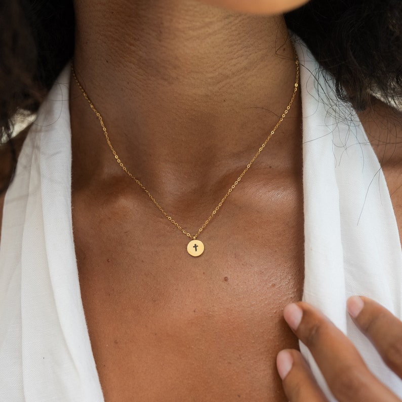 May include: A gold chain necklace with a small, round pendant featuring a cross design.