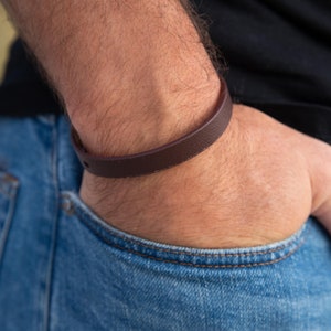 Può includere: Un braccialetto di pelle marrone indossato al polso.