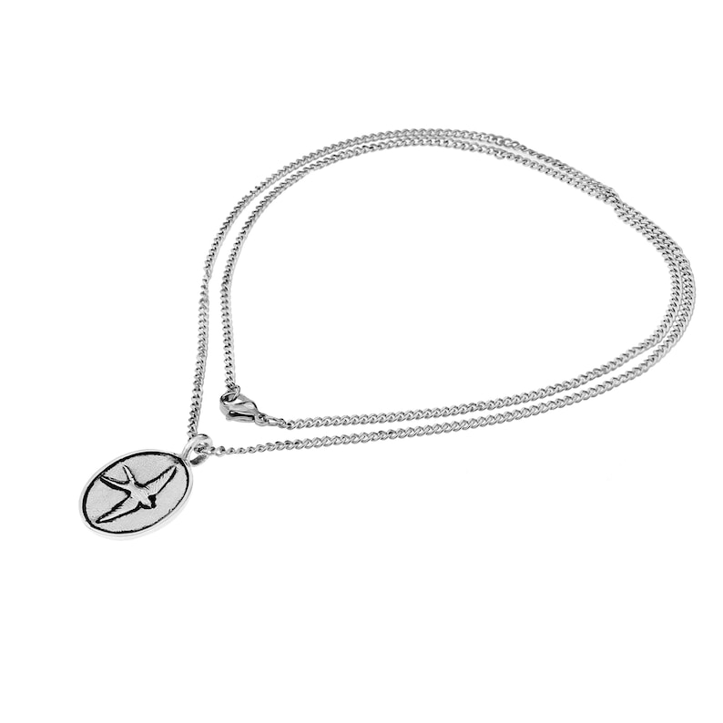 May include: A silver chain necklace with a silver oval pendant featuring a stylized bird design.