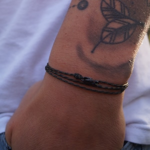 May include: A black paracord bracelet with a black metal clasp. The bracelet is worn on a person's wrist.