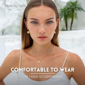 Op de afbeelding: Goudkleurige sieradenset met een ketting met een madeliefhanger en bijpassende oorbellen. De afbeelding bevat de tekst "COMFORTABLE TO WEAR" en "1 GR / 0.035 OZ LIGHTWEIGHT". De merknaam "Made by Nami" is ook zichtbaar.