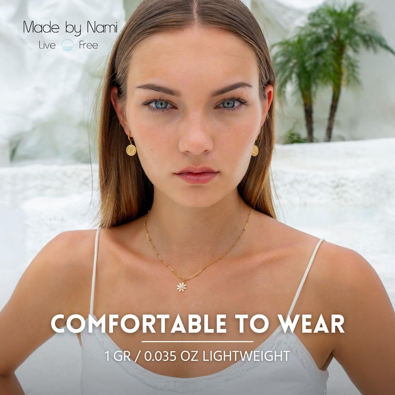 Op de afbeelding: Goudkleurige sieradenset met een ketting met een madeliefhanger en bijpassende oorbellen. De afbeelding bevat de tekst "COMFORTABLE TO WEAR" en "1 GR / 0.035 OZ LIGHTWEIGHT". De merknaam "Made by Nami" is ook zichtbaar.
