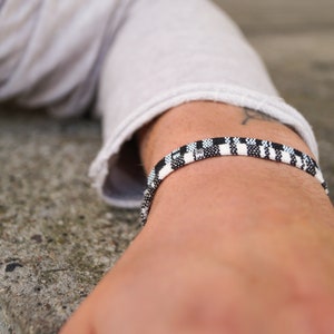 May include: A black and white checkered bracelet on a person's wrist.