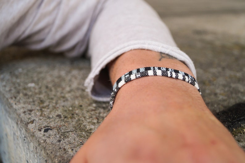 May include: A black and white checkered bracelet on a person's wrist.
