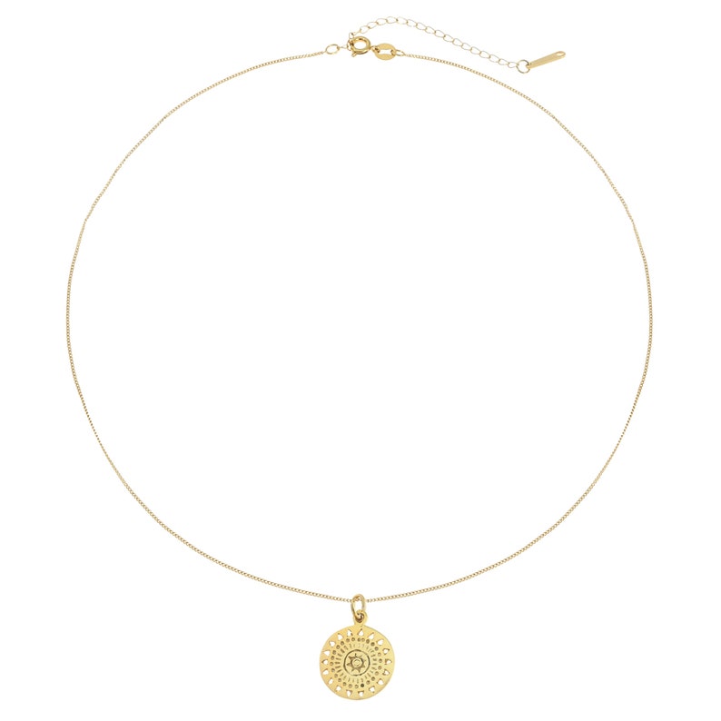 K&ouml;nnte beinhalten: Eine goldene Kettenkette mit einem zarten, runden Anh&auml;nger mit einem detaillierten, kreisf&ouml;rmigen Design.