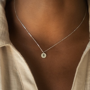 May include: A silver chain necklace with a small, round pendant featuring a cross cutout.