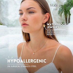 Op de afbeelding: Een vrouw draagt gouden sieraden, waaronder een ketting met een sterhanger en oorringen. De afbeelding bevat de tekst "Made by Nami", "Waterproof Jewelry" en "Hypoallergenic 316 Surgical Stainless Steel".