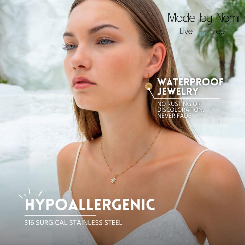 Op de afbeelding: Een vrouw draagt gouden sieraden, waaronder een ketting met een sterhanger en oorringen. De afbeelding bevat de tekst "Made by Nami", "Waterproof Jewelry" en "Hypoallergenic 316 Surgical Stainless Steel".