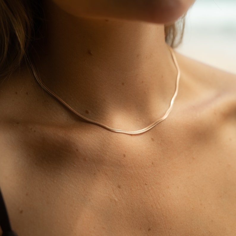 May include: A delicate gold chain necklace on a person's neck. The chain is thin and has a subtle shine.
