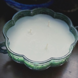 May include: A green, scalloped-edge candle holder with a white candle. The candle has three wicks. The holder has two handles and is made of a translucent green glass.