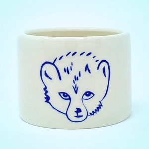 May include: White ceramic mug with a blue illustration of a bear's face.