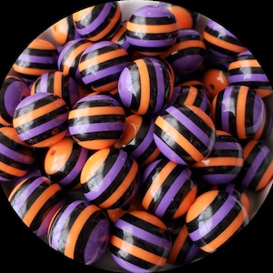 May include: A collection of orange and purple striped round beads. The beads are made of a glossy material and have a black stripe pattern.