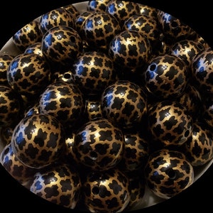 May include: A bowl of black and gold round beads with a geometric pattern. The beads are made of plastic and have a glossy finish.