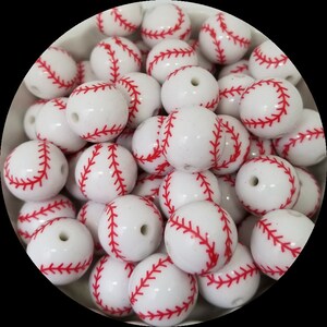 May include: A collection of white baseball-themed beads with red stitching. These round beads have a glossy finish and a hole for stringing. The beads are ideal for crafting projects and jewelry making.
