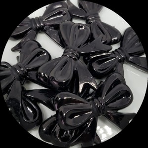 May include: A group of black plastic bows with a glossy finish. The bows are arranged in a circle on a white background.