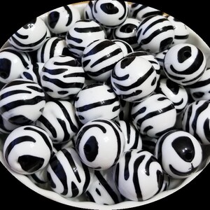 May include: A bowl filled with black and white zebra print round beads. The beads are glossy and have a smooth finish.
