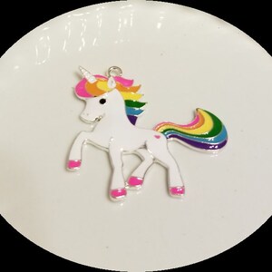 May include: A white unicorn charm with a rainbow mane and tail. The unicorn has pink hooves and a pink heart on its side.