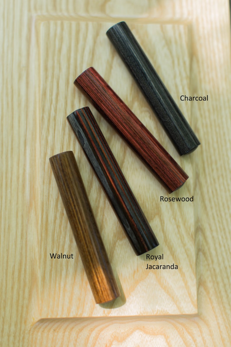 K&ouml;nnte beinhalten: Vier Holzstift in verschiedenen Holzarten: Walnuss, Palisander, Royal Jacaranda und Holzkohle. Die Stifte sind f&auml;cherf&ouml;rmig auf einer hellen Holzoberfl&auml;che angeordnet.