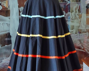 May include: A full circle skirt in black with colourful ribbon trim. The skirt is on a dress form and has a fitted black top.