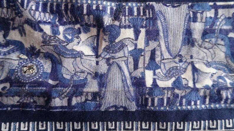 May include: Blue and white fabric with a repeating pattern of stylised figures and geometric designs. The fabric has a textured surface and a dark blue border.