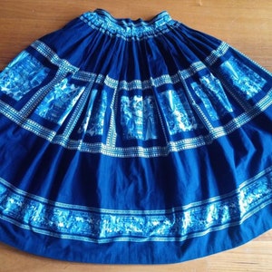 May include: A full blue skirt with a white and blue patterned design. The skirt has a gathered waist and a full, flowing silhouette.