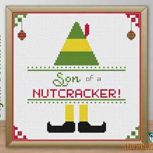 May include: Cross stitch pattern featuring a green and yellow elf hat with the text "Son of a Nutcracker!" in red and green.