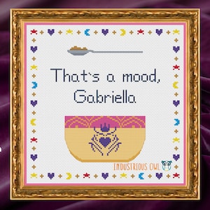 Può includere: Schema di punto croce con una ciotola gialla con un bordo rosa e un design a corona e cuore viola. Il testo "That's a mood, Gabriella" è sopra la ciotola. Lo schema è incorniciato in una cornice dorata con un passepartout rosa.