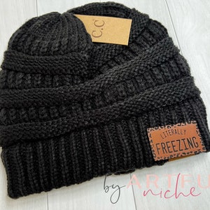 May include: Black knit beanie with a brown leather patch that says "Literally Freezing".