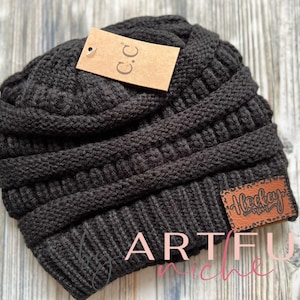 May include: Black knitted beanie with a brown leather patch that says "Hockey Mom".