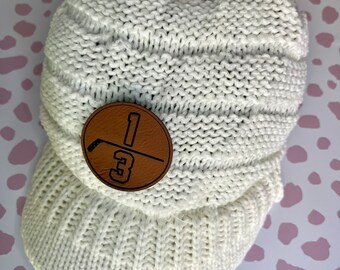 May include: White knitted beanie with a brown leather patch featuring a hockey stick and the number "13".