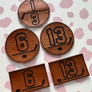 May include: Four brown leather patches with black hockey numbers and a hockey stick graphic. The numbers are 13, 6, 13, and 6.