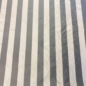 May include: A fabric with a repeating pattern of vertical stripes. The stripes alternate between a light gray and white color. The fabric has a smooth texture and appears to be lightweight.