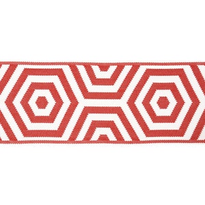 Op de afbeelding: Een close-up van een rood en wit geometrisch patroon tapijt. Het tapijt heeft een herhalend patroon van rode zeshoeken met witte contouren en binnenste vormen. Het tapijt is gemaakt van een geweven materiaal.