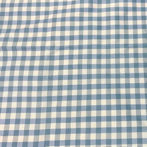 Op de afbeelding: Een stof met een klassiek gingham-patroon met afwisselende vierkanten in gedempt blauw en gebroken wit. Het textiel vertoont een consistent, herhalend rasterontwerp over het gehele oppervlak, met een geweven textuur met zichtbare draadlijnen.