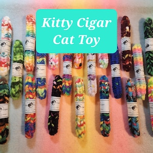 May include: A collection of 24 colorful cat toys shaped like cigars. Each toy is made of soft, fuzzy material and has a label that reads "Kitty Cigar".
